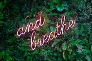 "and breathe" neon pink sign on a wall of plants